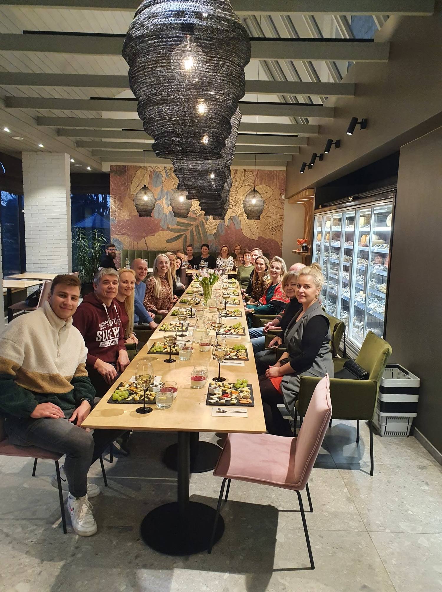 Didelė grupė šypsosi prie ilgo degustacijos stalo